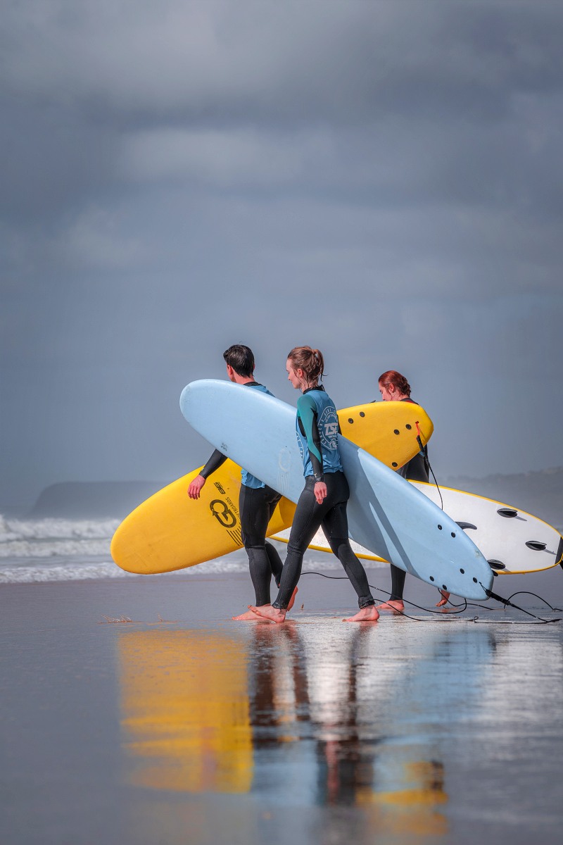 people learning surfing and carrying their surfboard